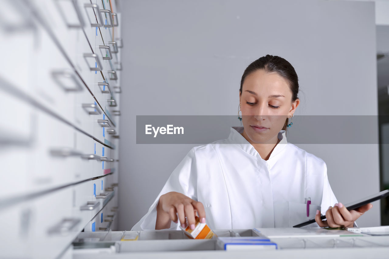 Woman wearing lab coat while looking in drawer of cabinet