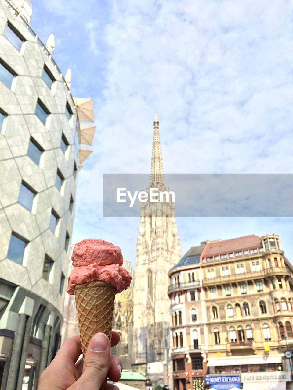 Cropped image of hand holding ice cream cone against st stephens cathedral