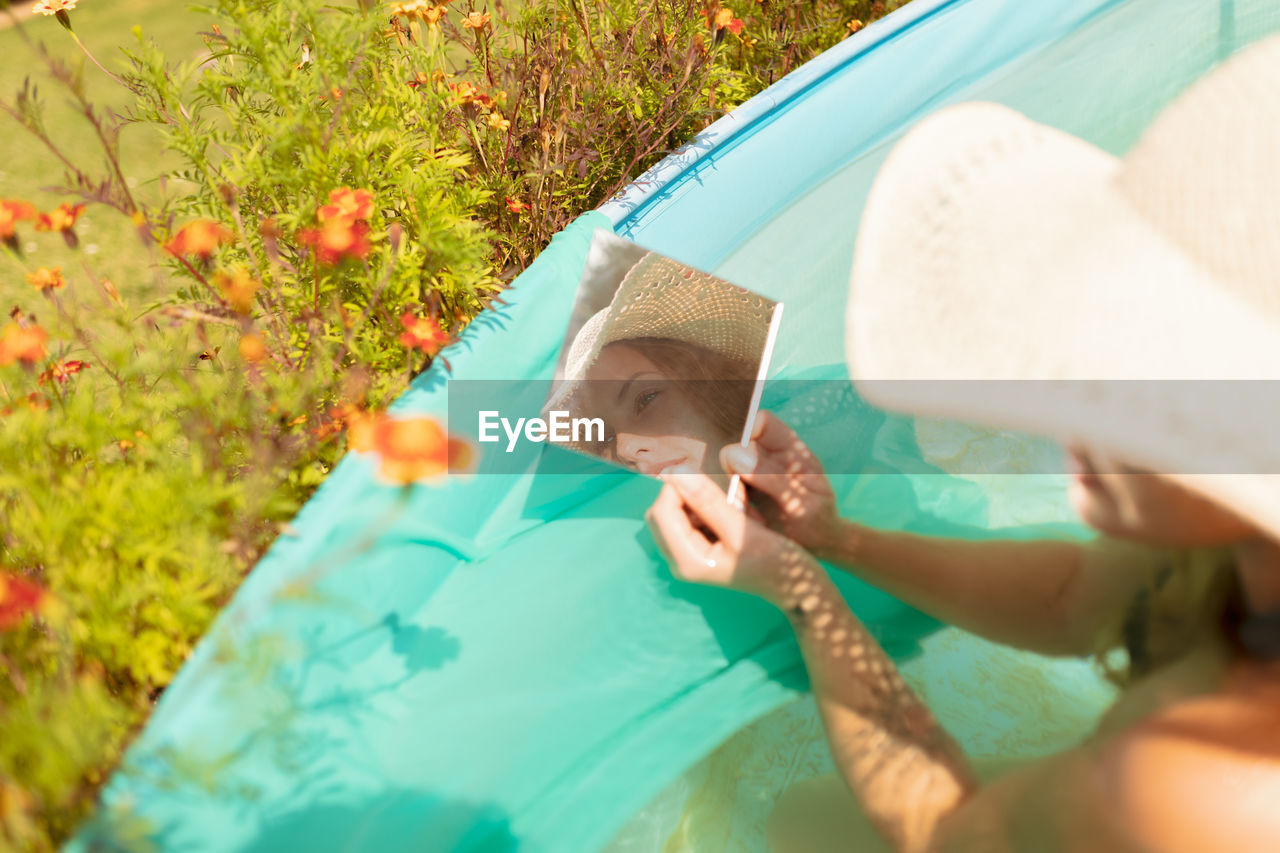 Young woman holding mirror with reflection in wading pool