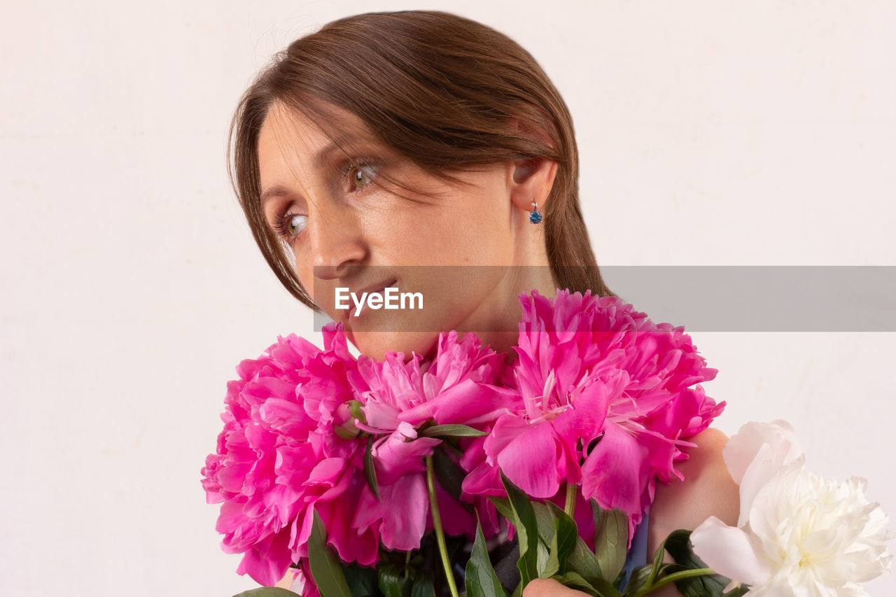 Portrait of a thoughtful young woman with a bouquet of peonies close-up