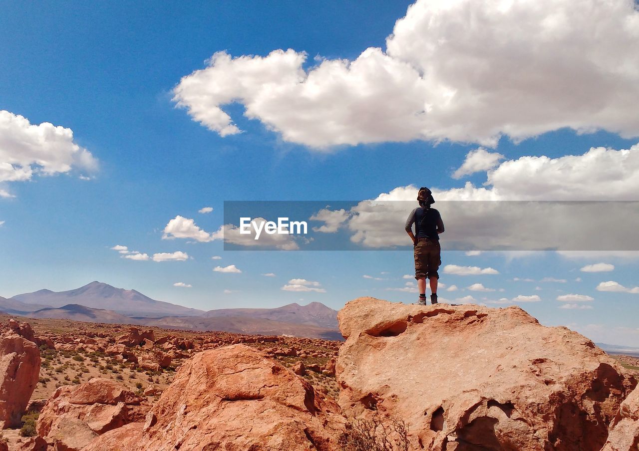 Woman standing on rock looking at mountains against sky