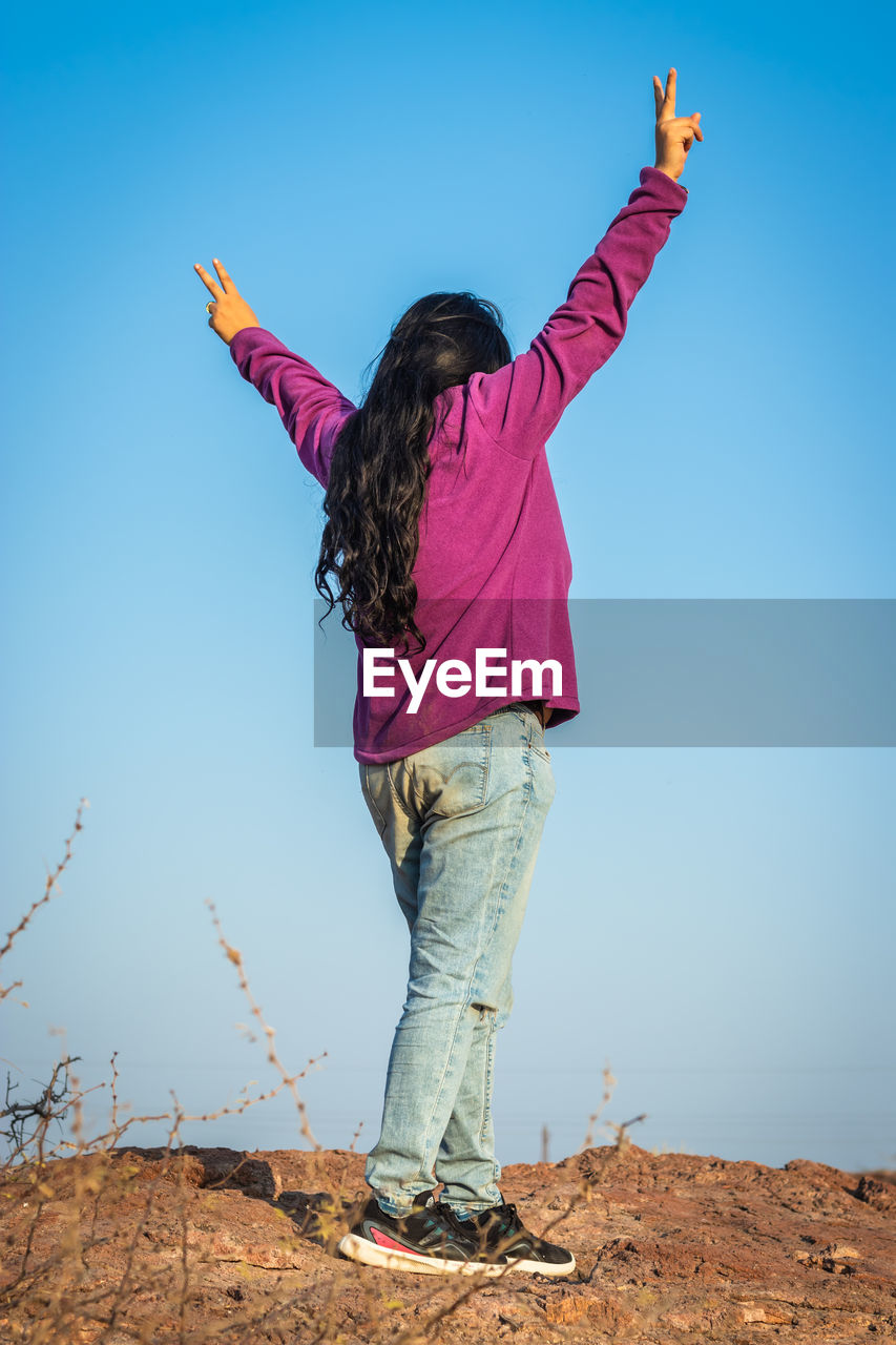 Isolated young girl standing at mountain top with blue sky from flat angle