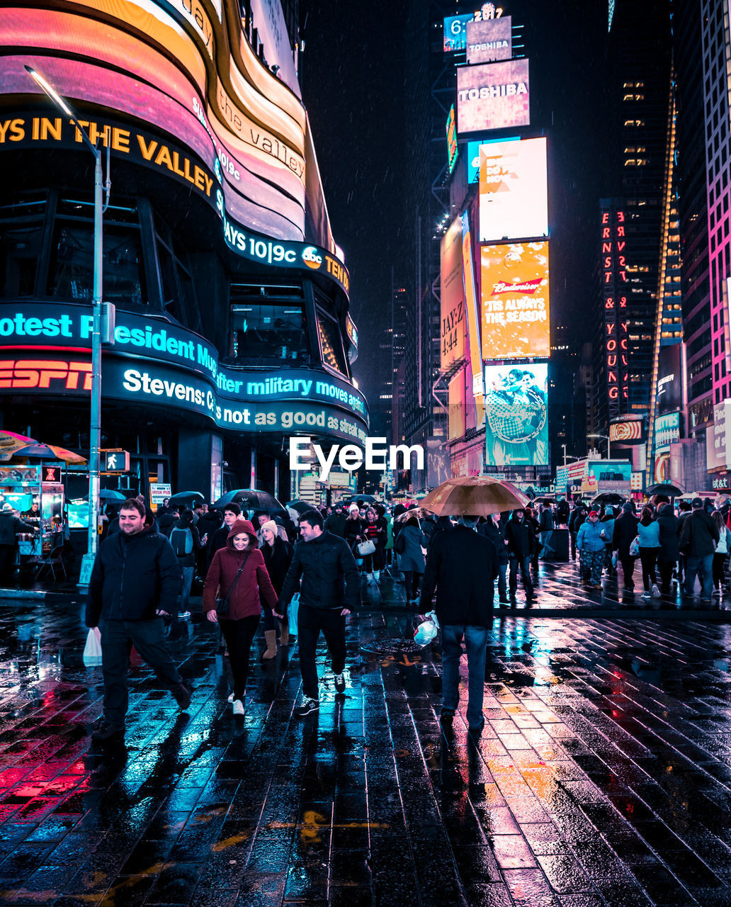 CROWD WALKING IN ILLUMINATED CITY AT NIGHT