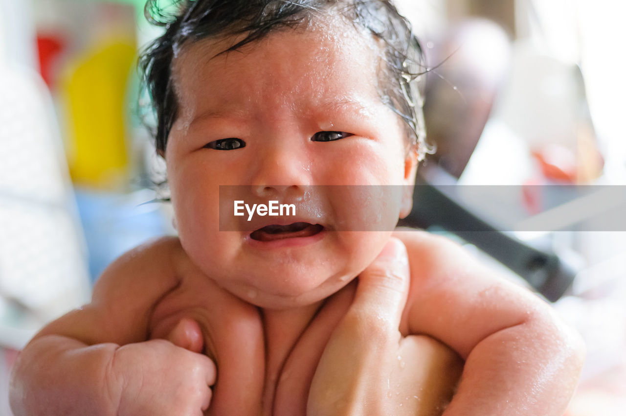 Cropped hand holding crying baby girl while taking bath