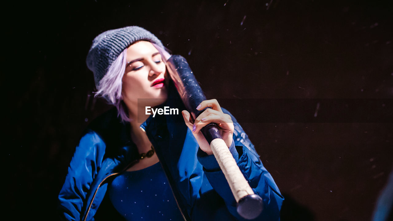 Young woman with baseball bat standing outdoors at night