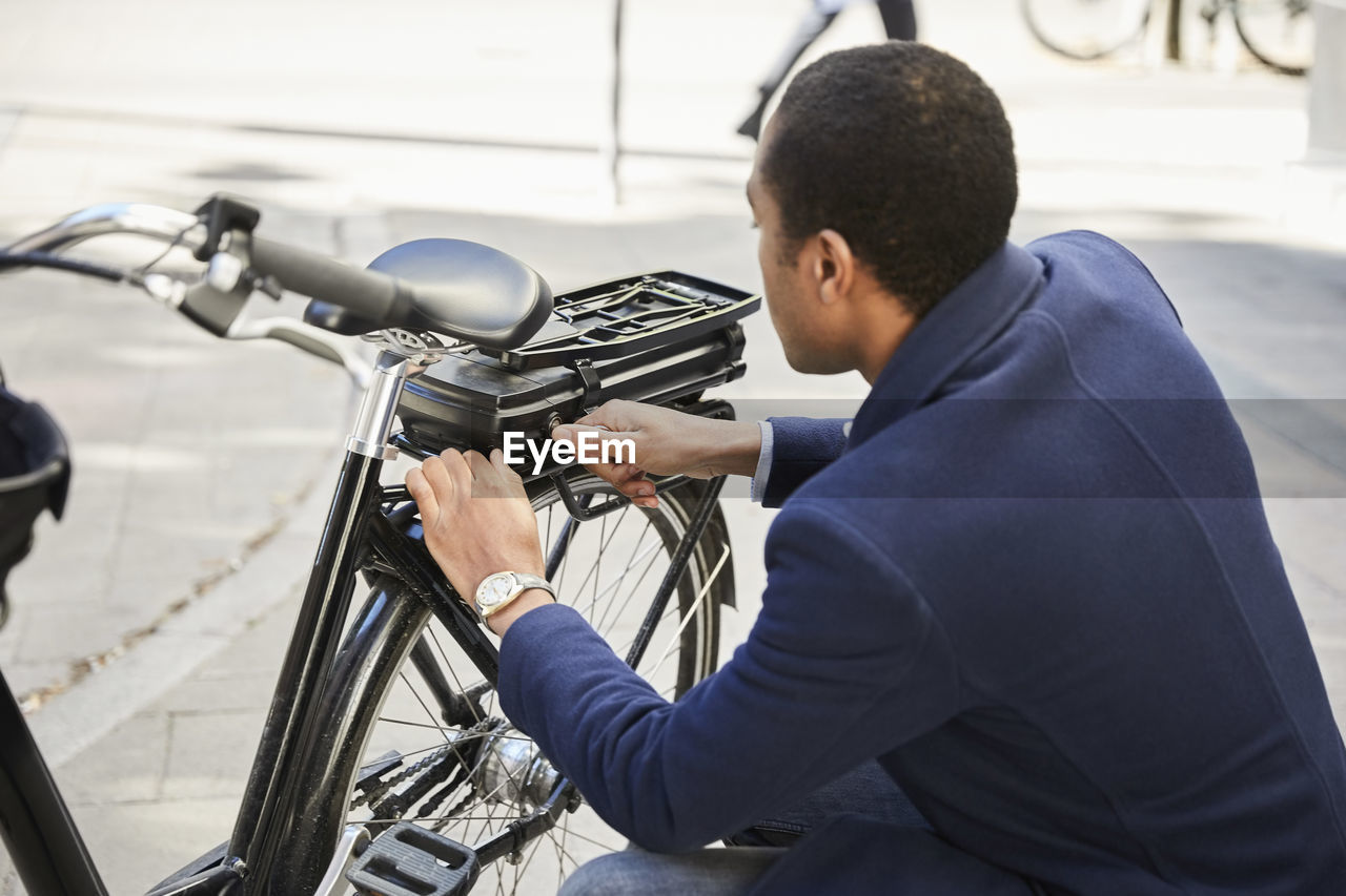 Young male commuter locking electric bicycle in city