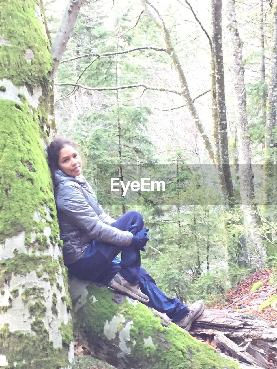 Side view portrait of woman sitting on mossy tree trunk in forest