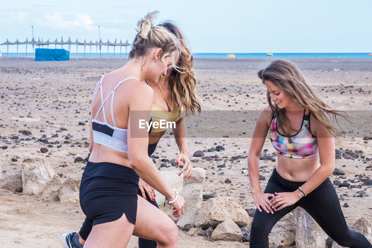 Friends exercising at beach against sky