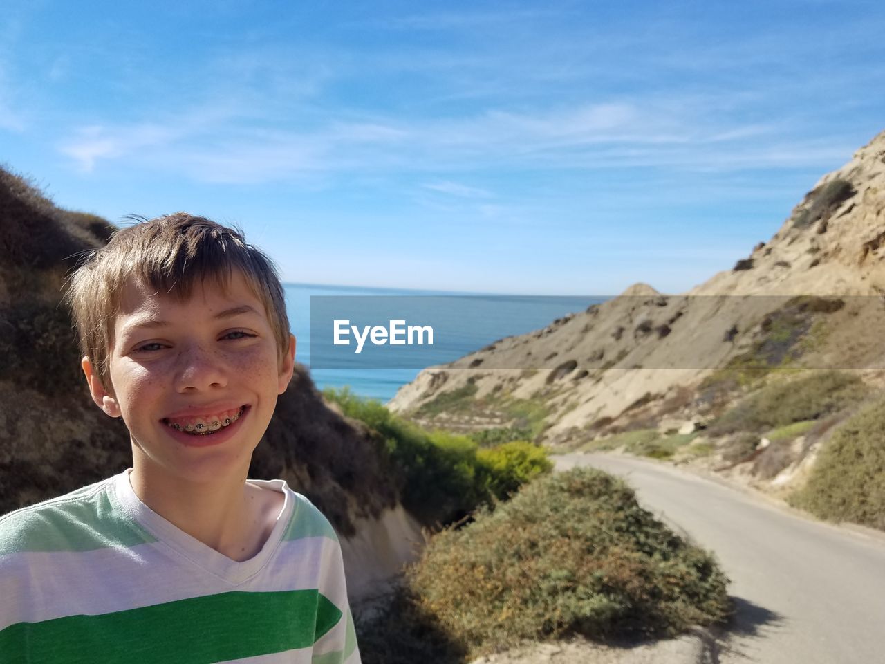 Portrait of smiling boy by mountain road against sky