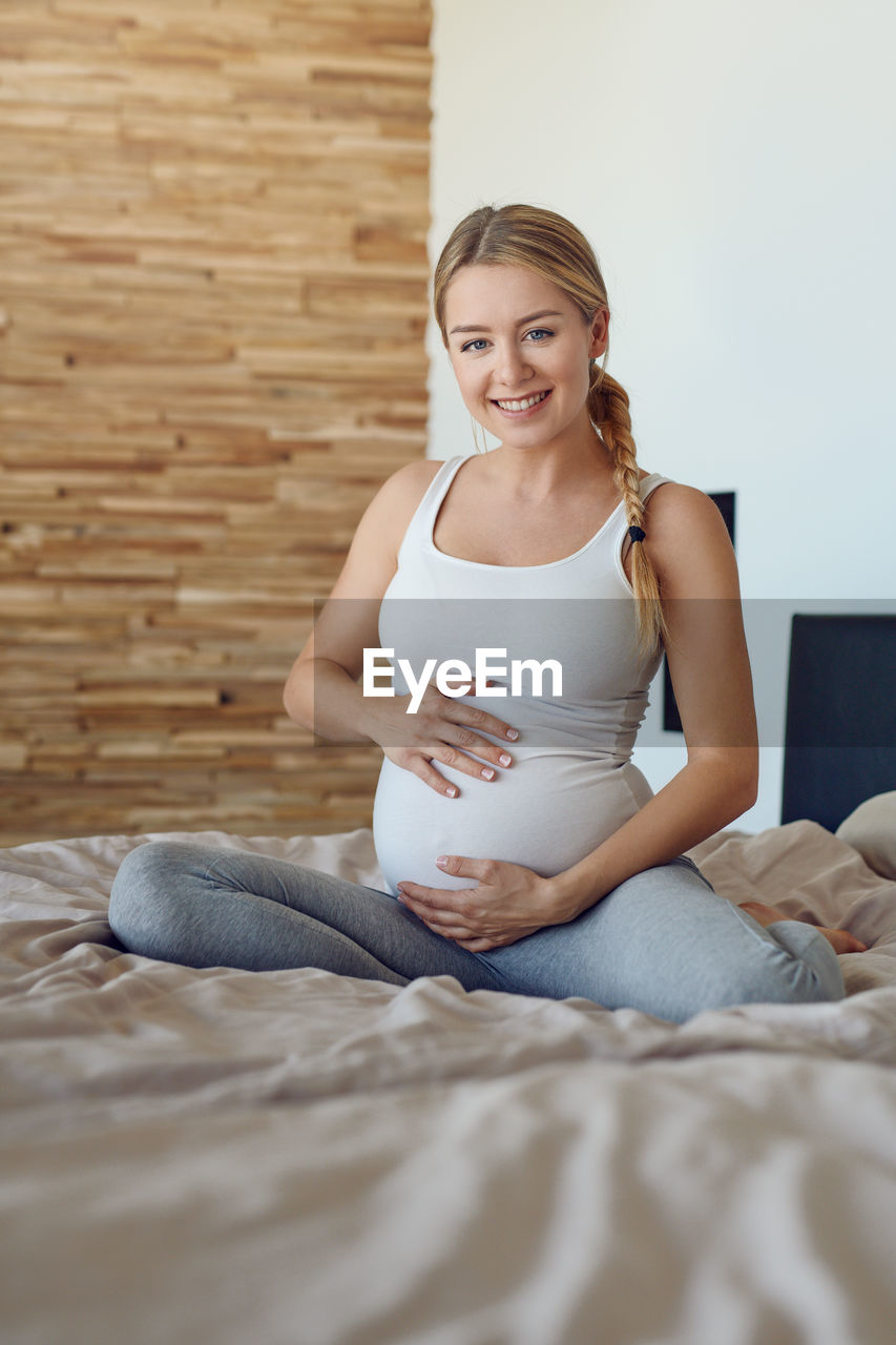 Portrait of smiling pregnant woman sitting on bed at home