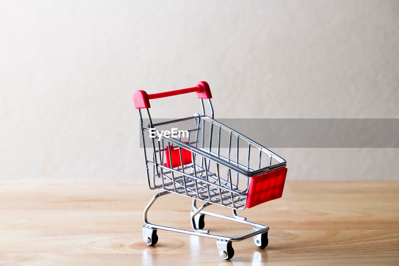 Close-up of shopping cart on wooden table against wall