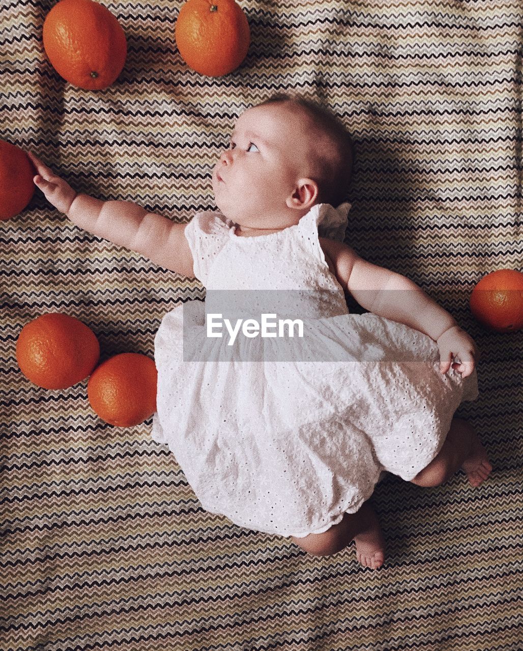 Baby girl wearing a princess dress laying on a mat trying to reach an orange 