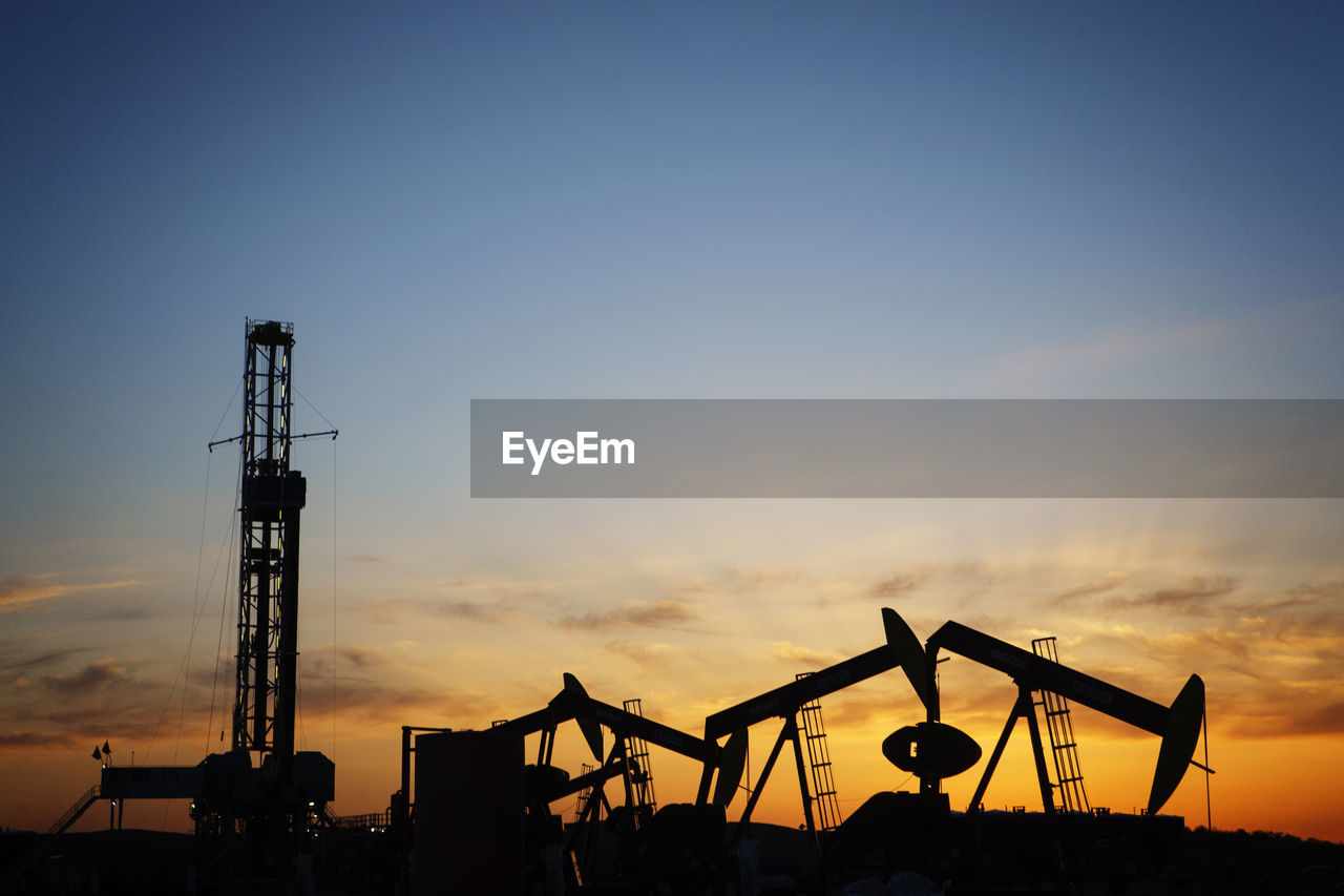 Silhouette oil pumps on field against sky during sunset