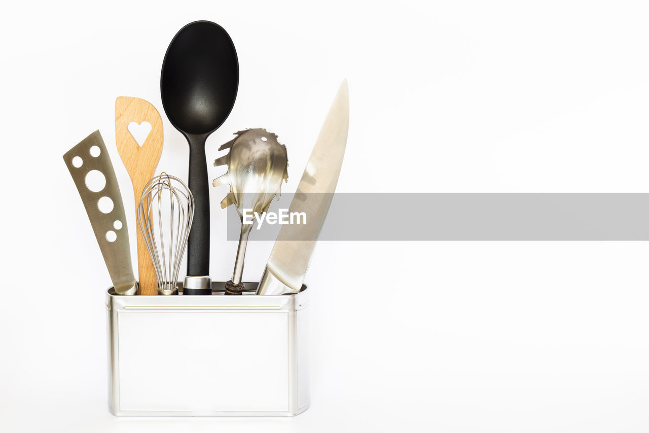 Kitchen utensils in container against white background