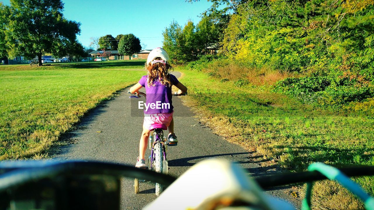 Rear view of girl riding bicycle on road amidst grass
