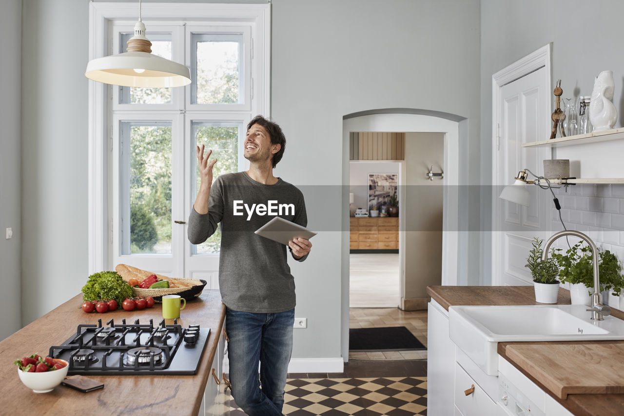 Happy man using tablet in kitchen looking at ceiling lamp