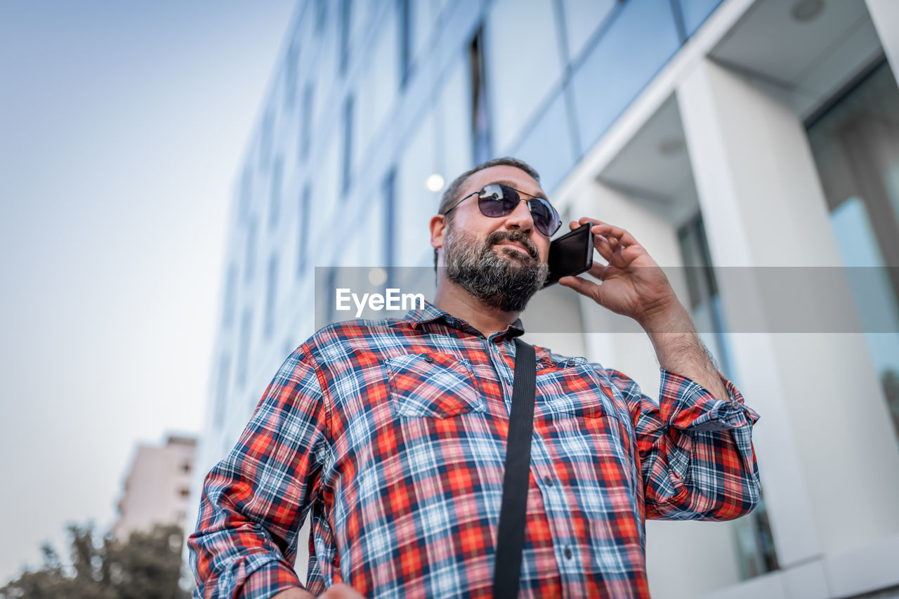 Portrait of handsome businessman with sunglasses and plaid shirt walking in the street
