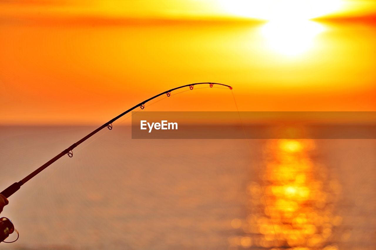 FISHING ROD OVER SEA AGAINST ORANGE SKY