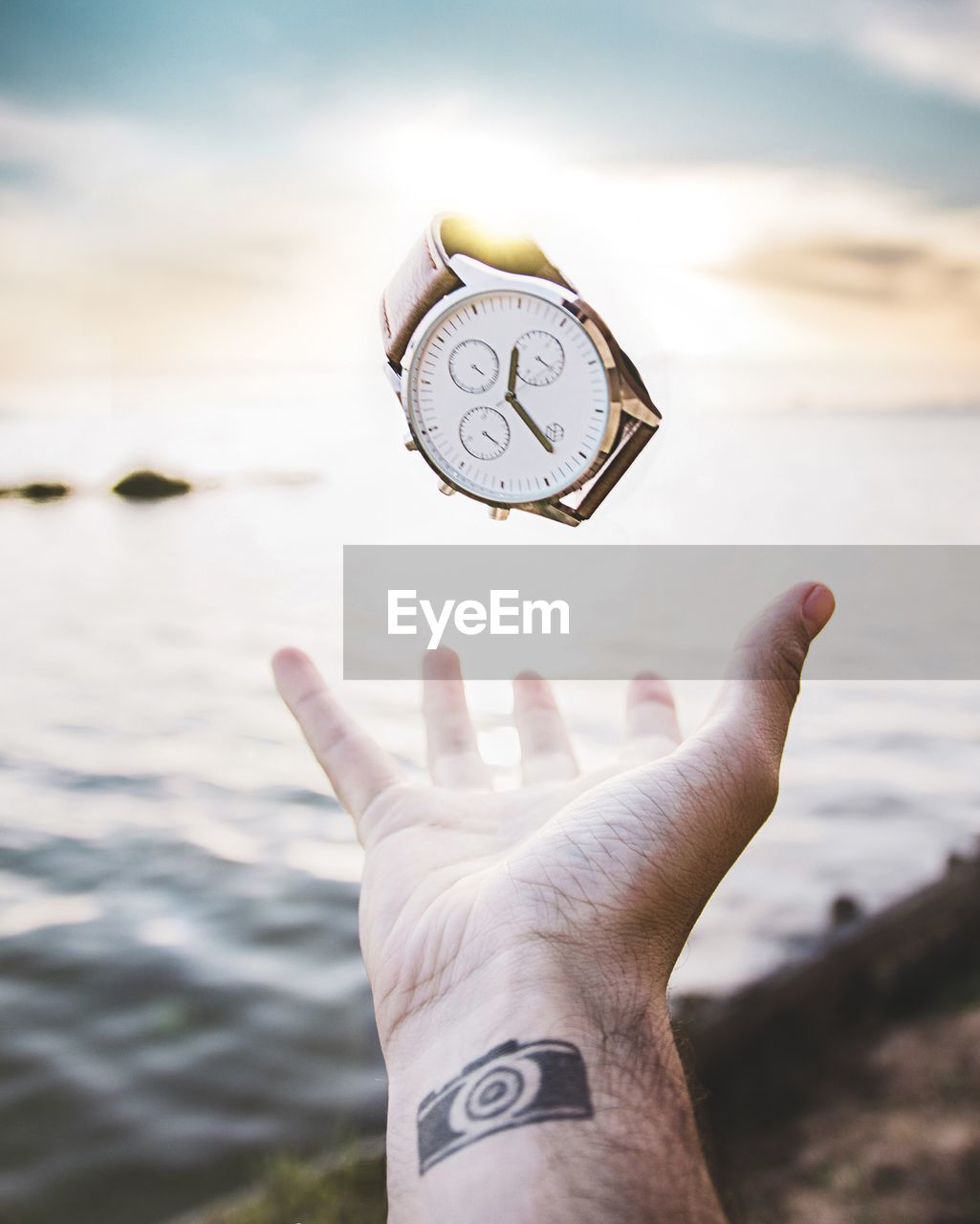 Close-up of hand holding wristwatch against sea and sky