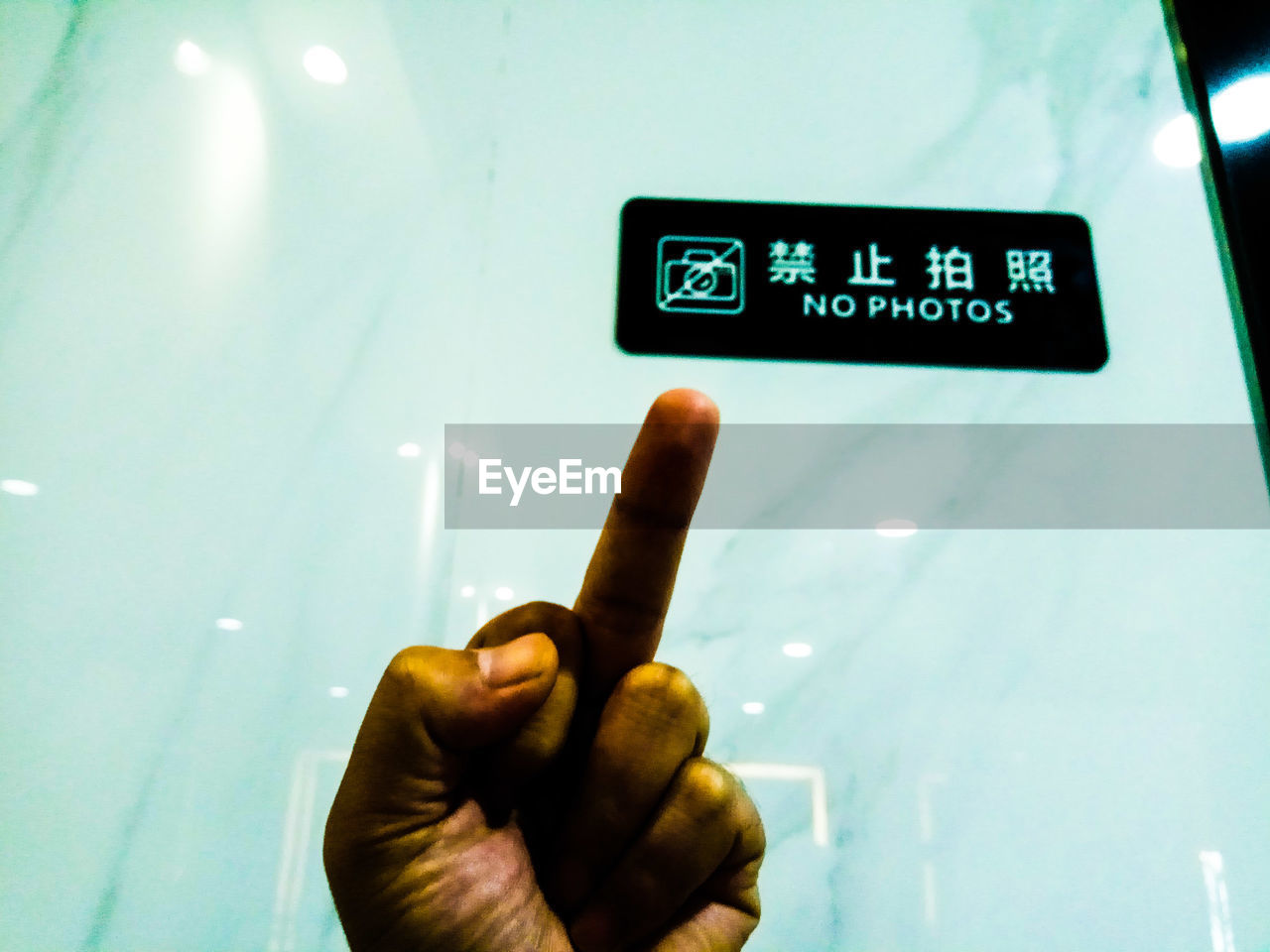 Close-up of hand showing middle finger against sign board