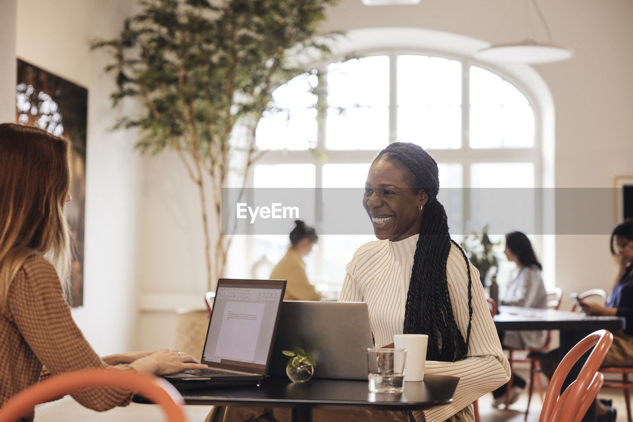 Happy female entrepreneur talking with colleague working on laptop at office