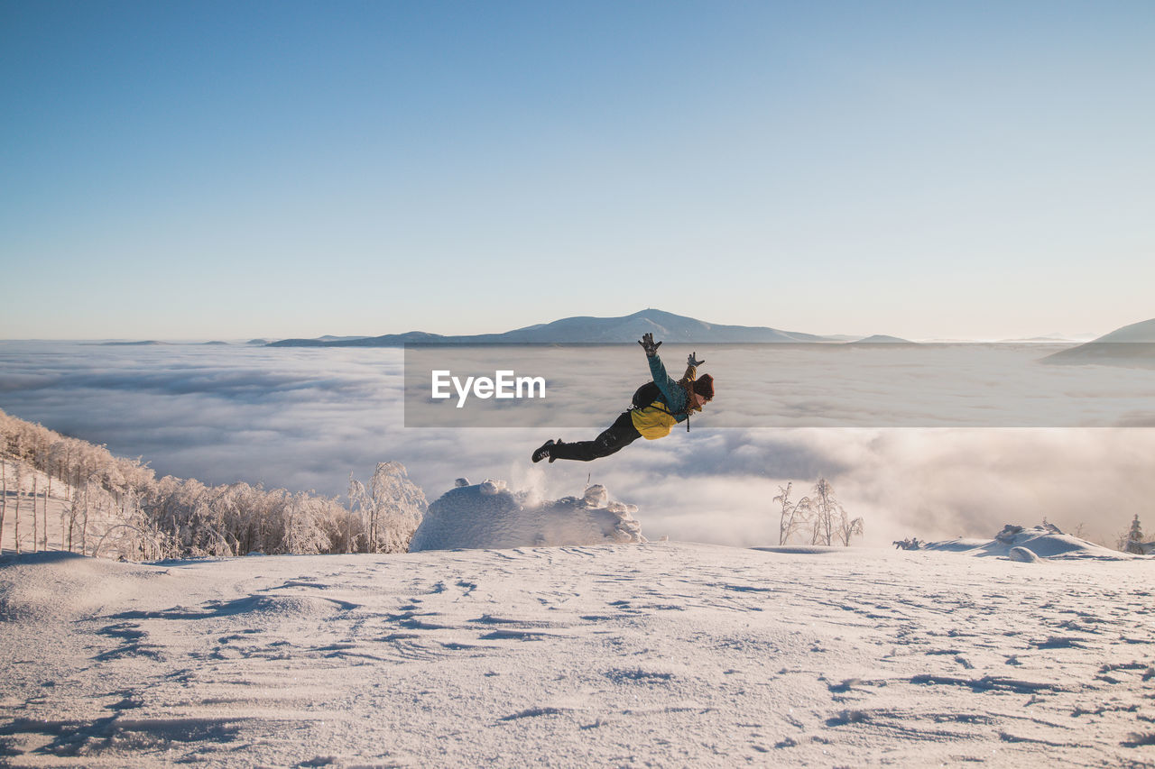 Energetic boy in winter clothes jumping from a stump into the fresh snow with a view of the sunrise