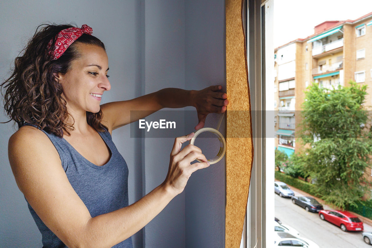 Woman holding adhesive tape by window at home