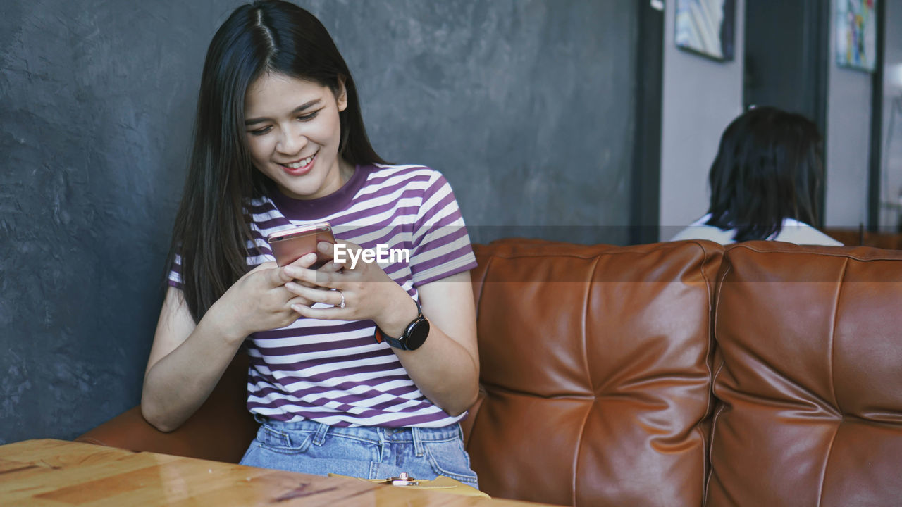 Smiling young woman using smart phone sitting at table in cafe