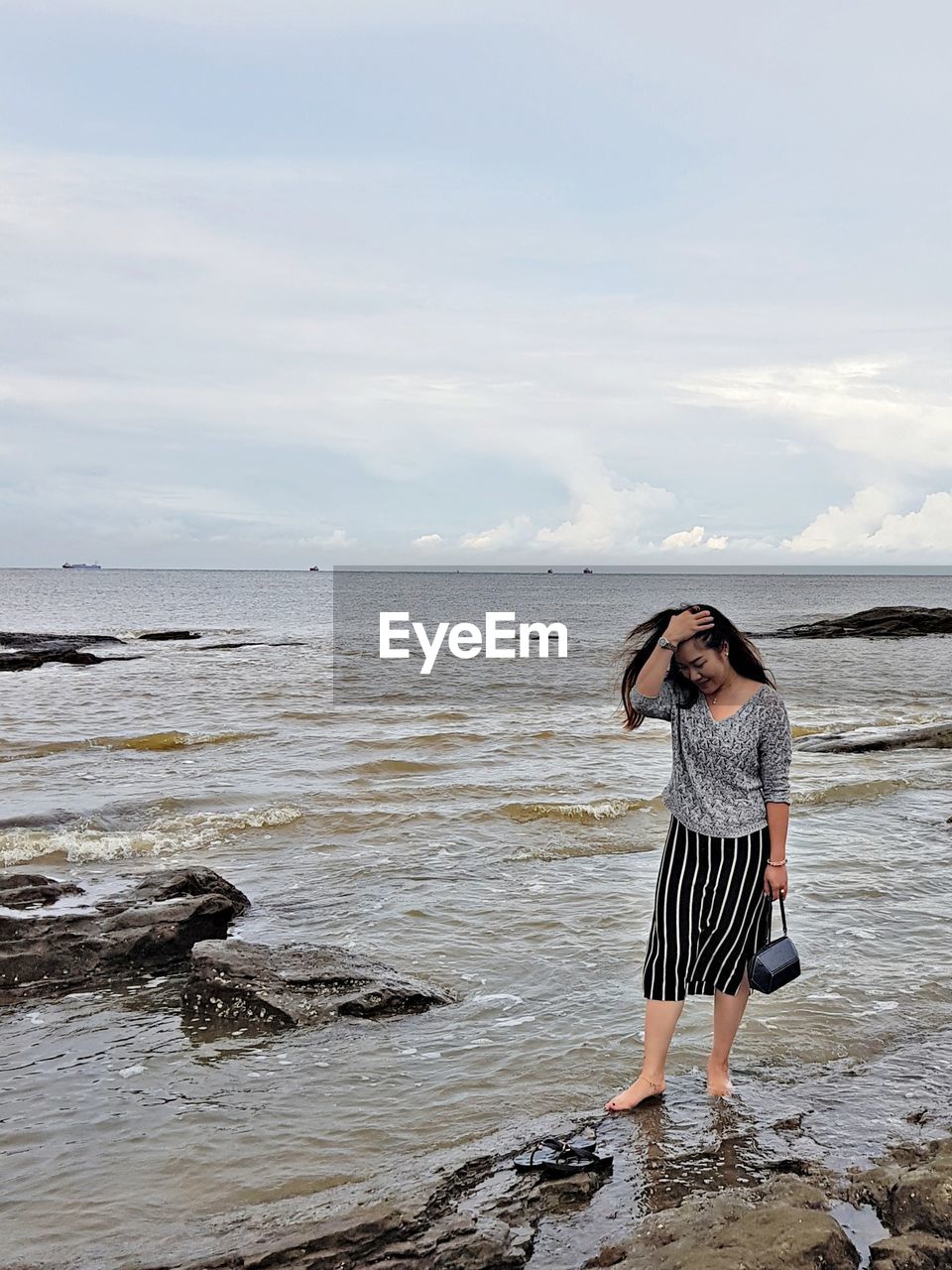 Woman standing at beach against cloudy sky