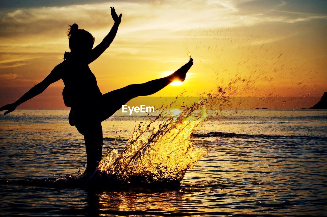 Silhouette woman in calm sea at sunset