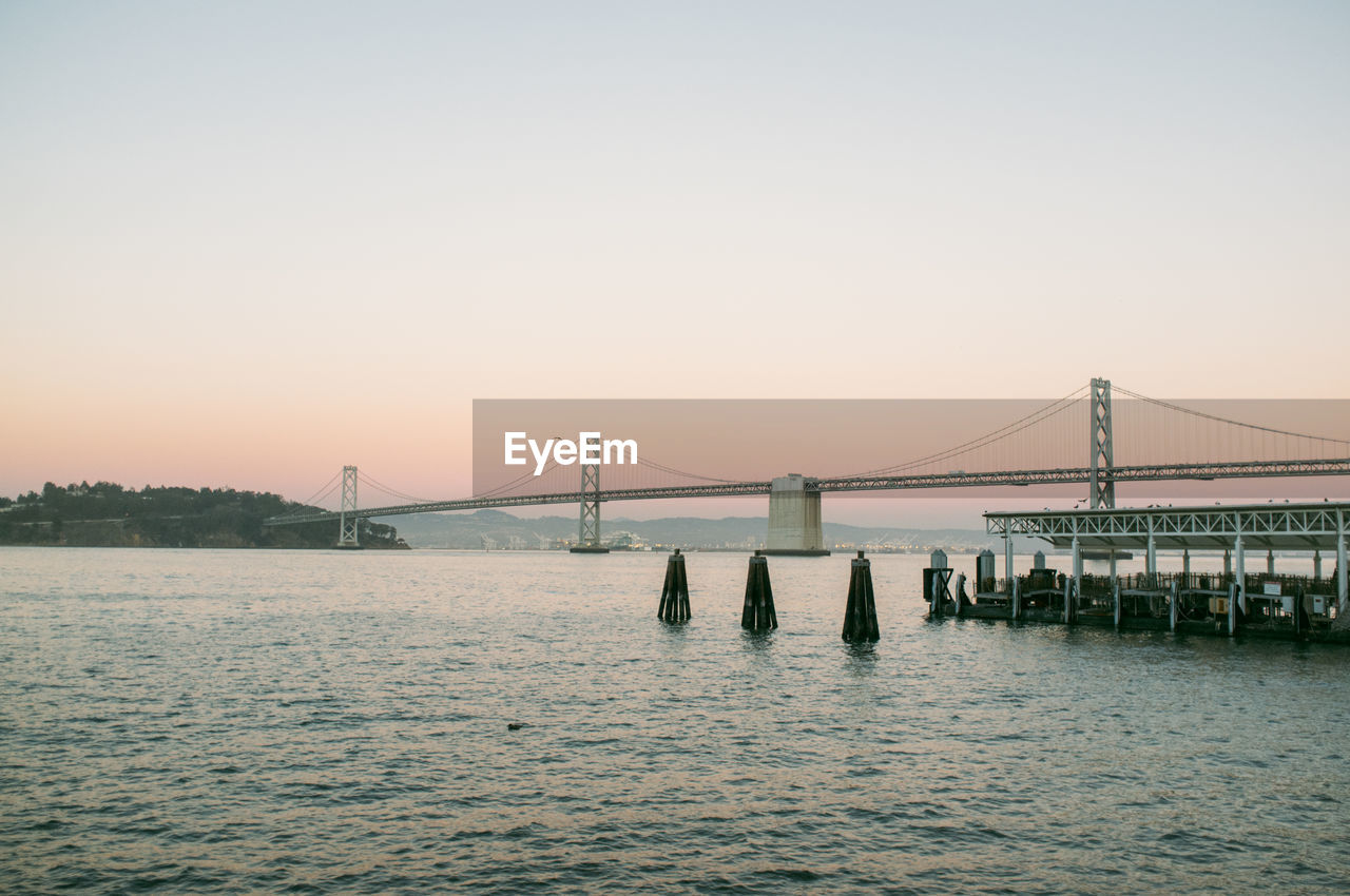 Oakland bay bridge over water against sunset sky
