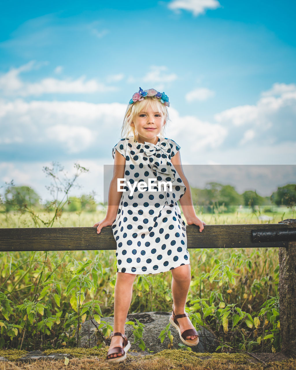 Portrait of girl sitting on railing against blue sky