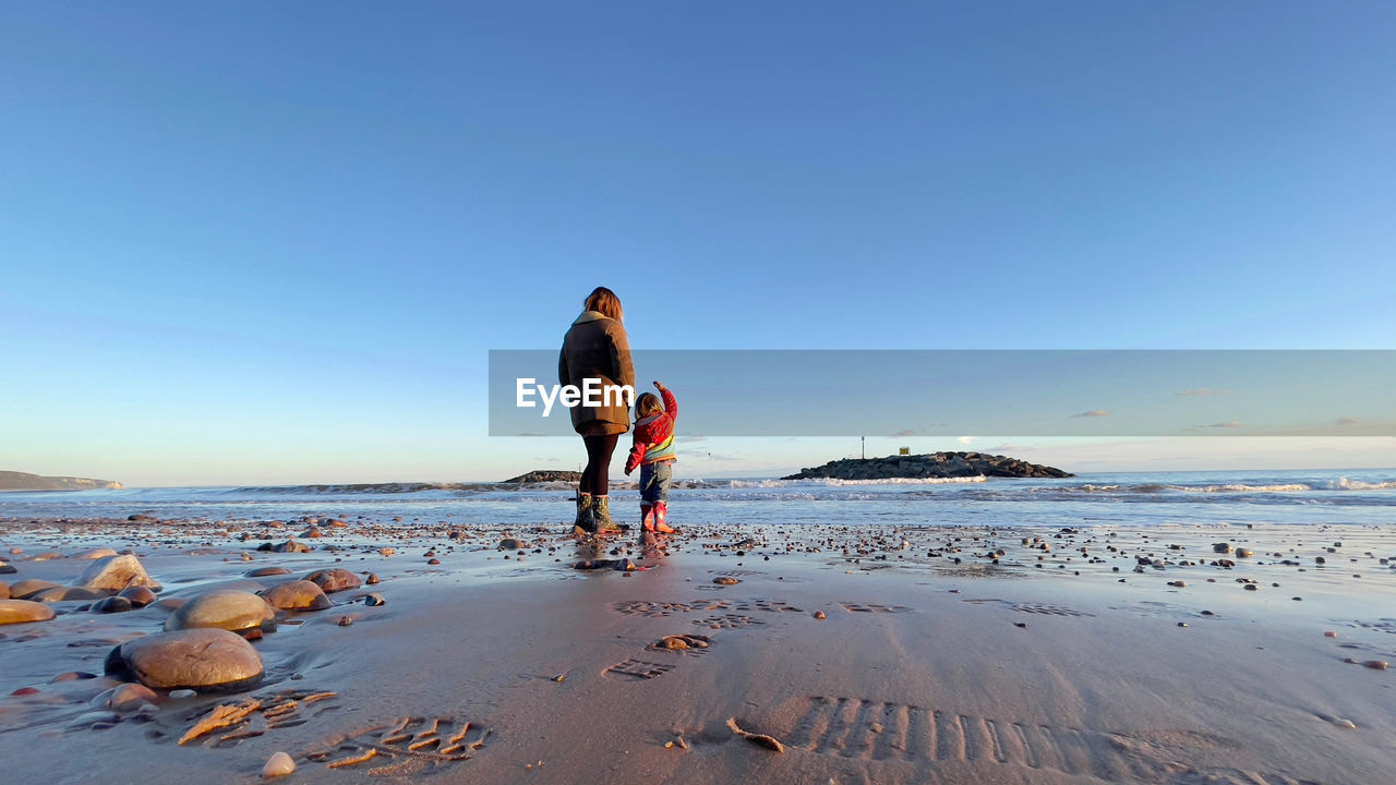 REAR VIEW OF WOMEN ON BEACH AGAINST SKY