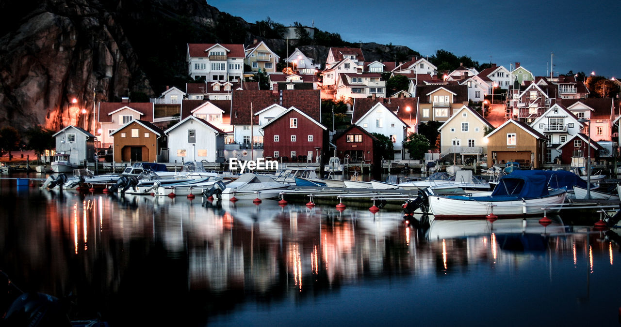 Boats moored on sea against houses at dusk