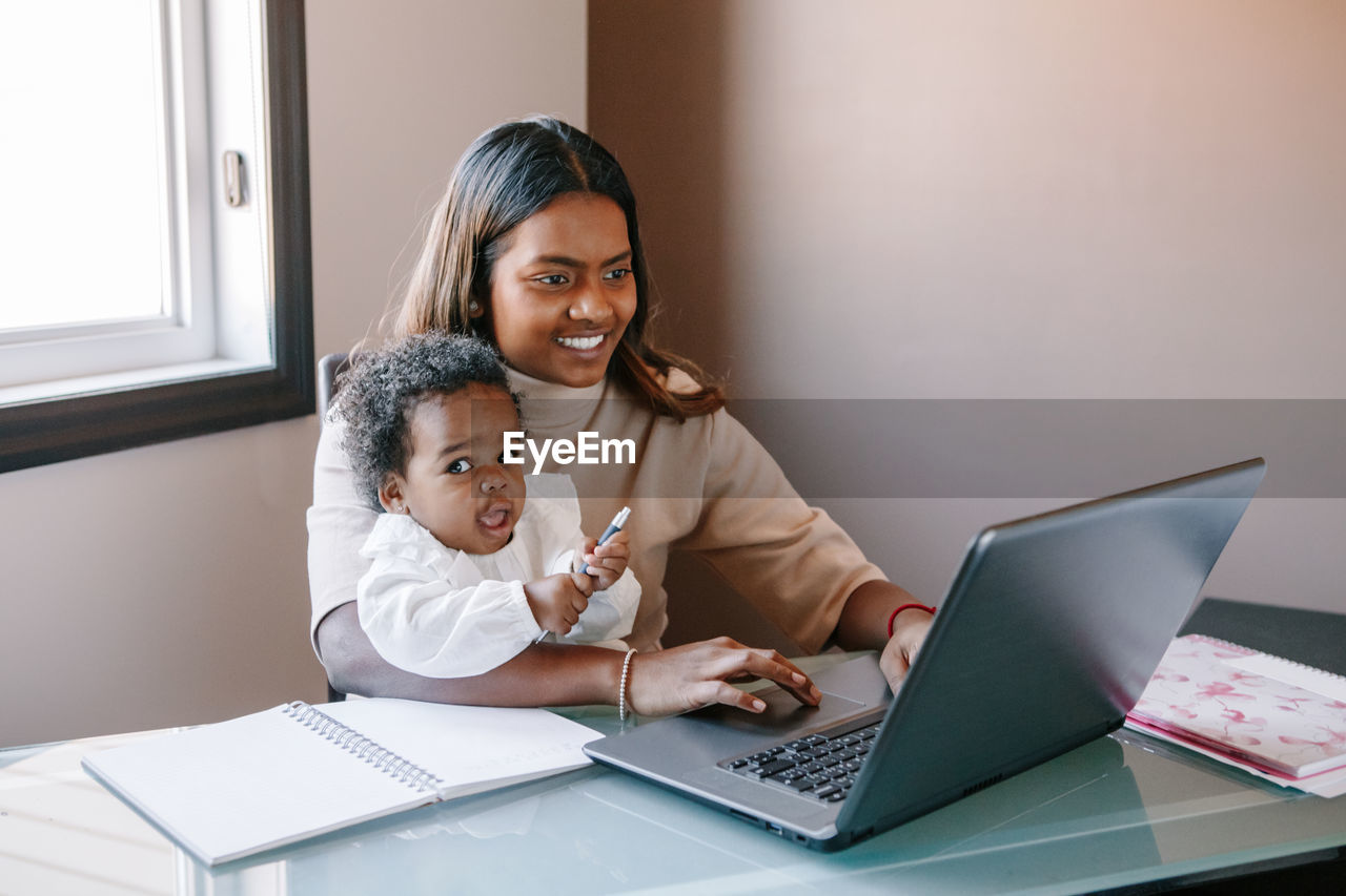 Mixed race indian mother with african black baby working online from home. workplace of freelancer 