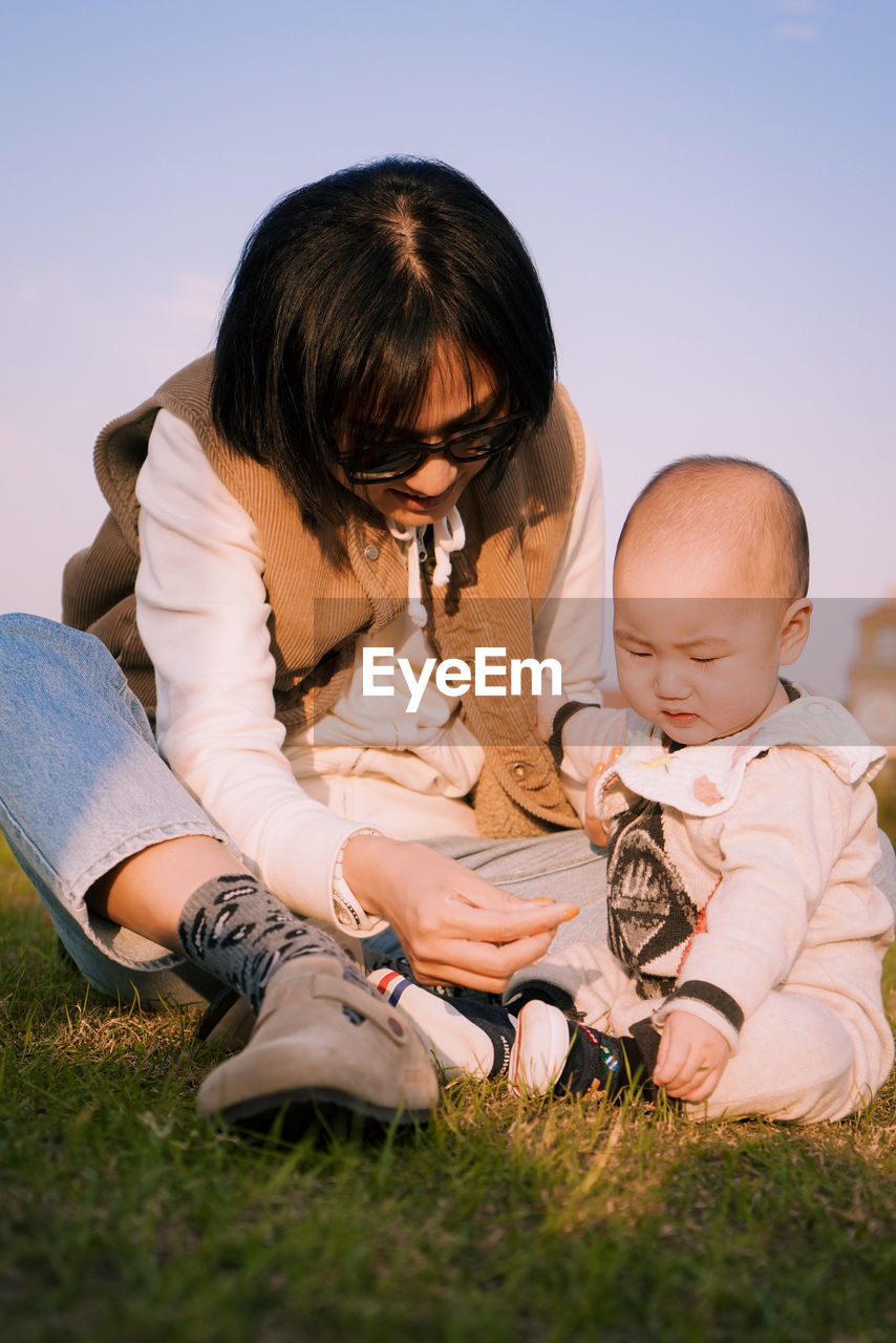 side view of mother and daughter sitting on grassy field