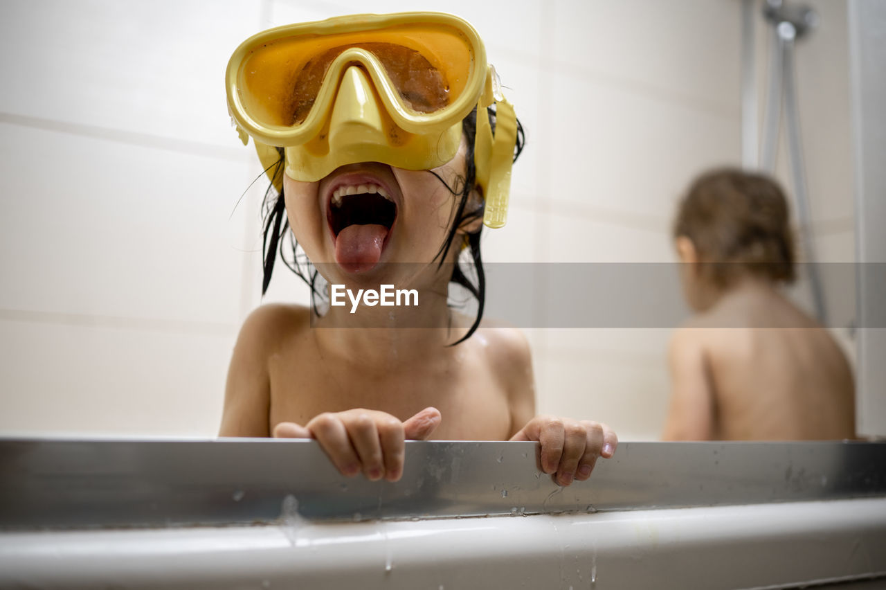 Boy wearing swimming goggles taking bath in bathroom