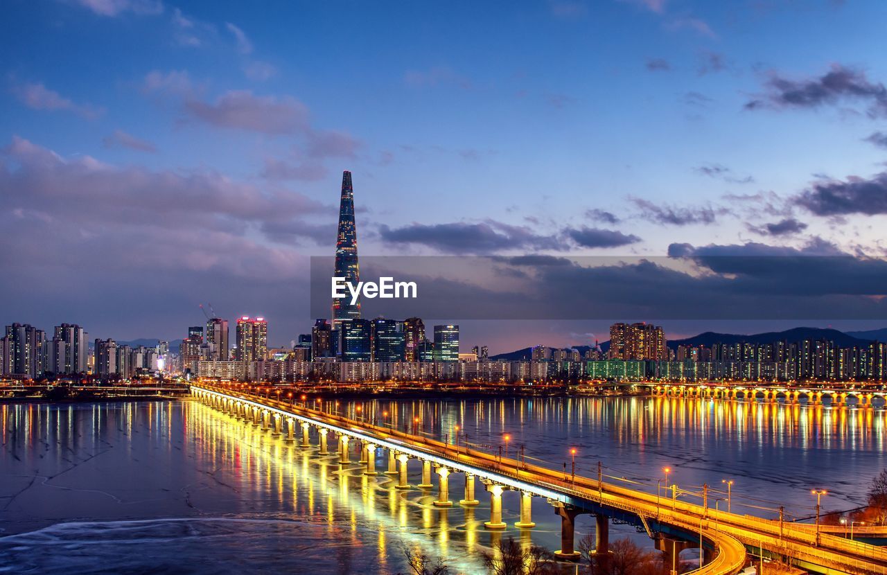 Illuminated buildings by sea against sky at night