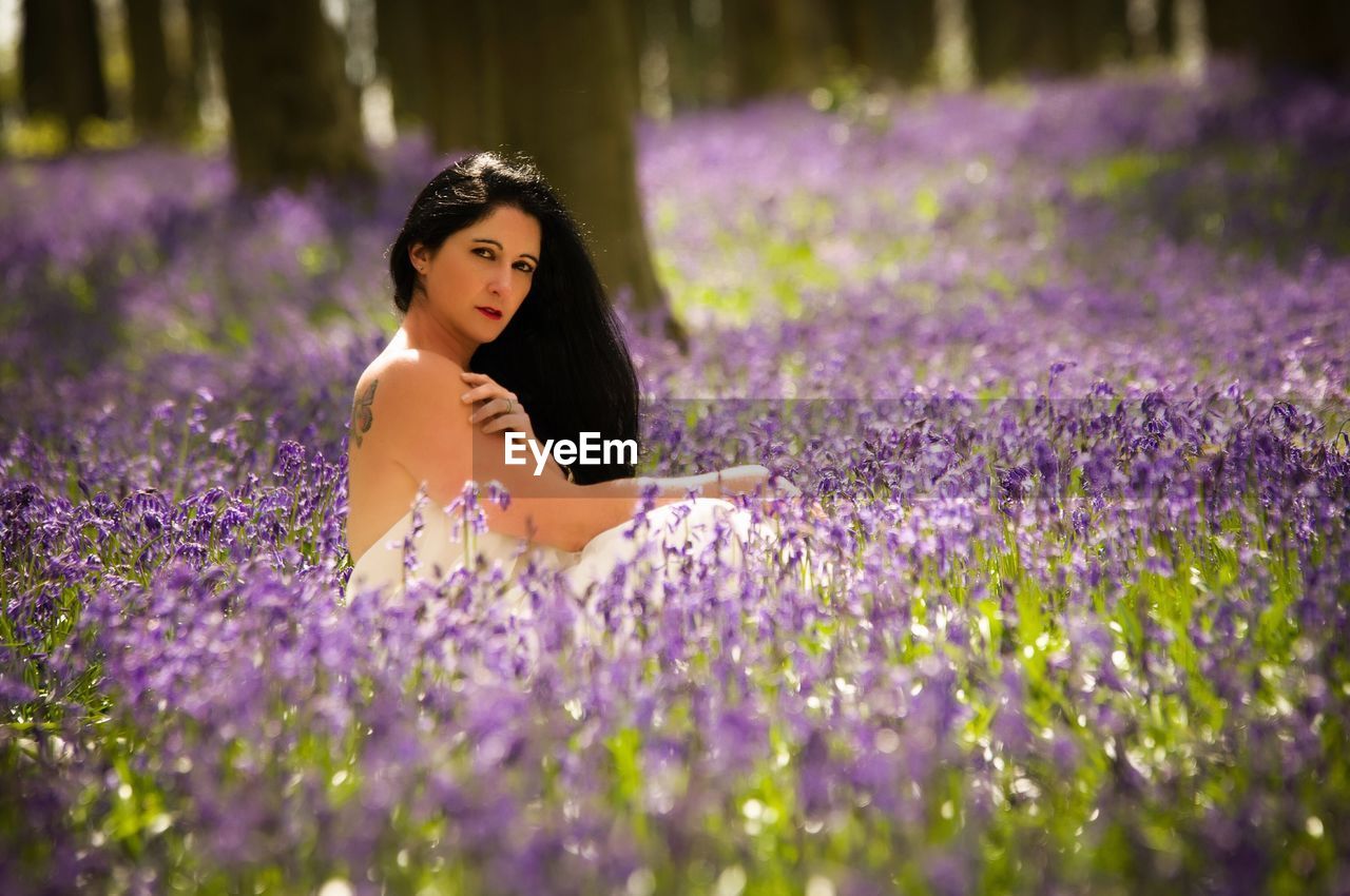 Portrait of woman sitting amidst purple flowers on field