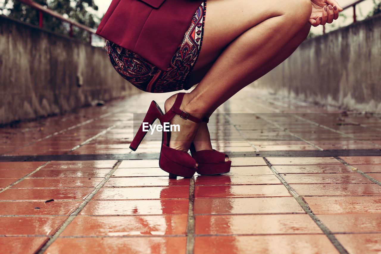 Low section of woman with high heels crouching on street