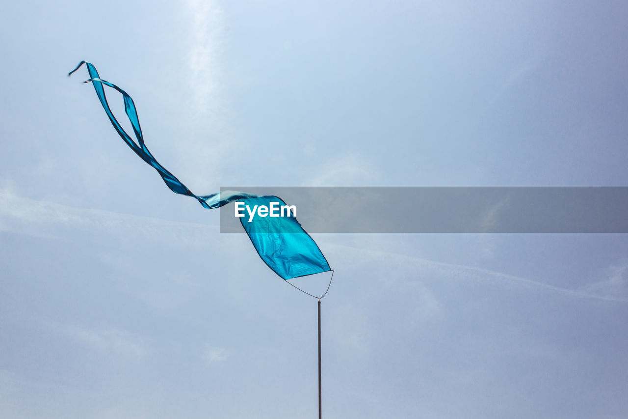 Low angle view of blue textile waving against sky