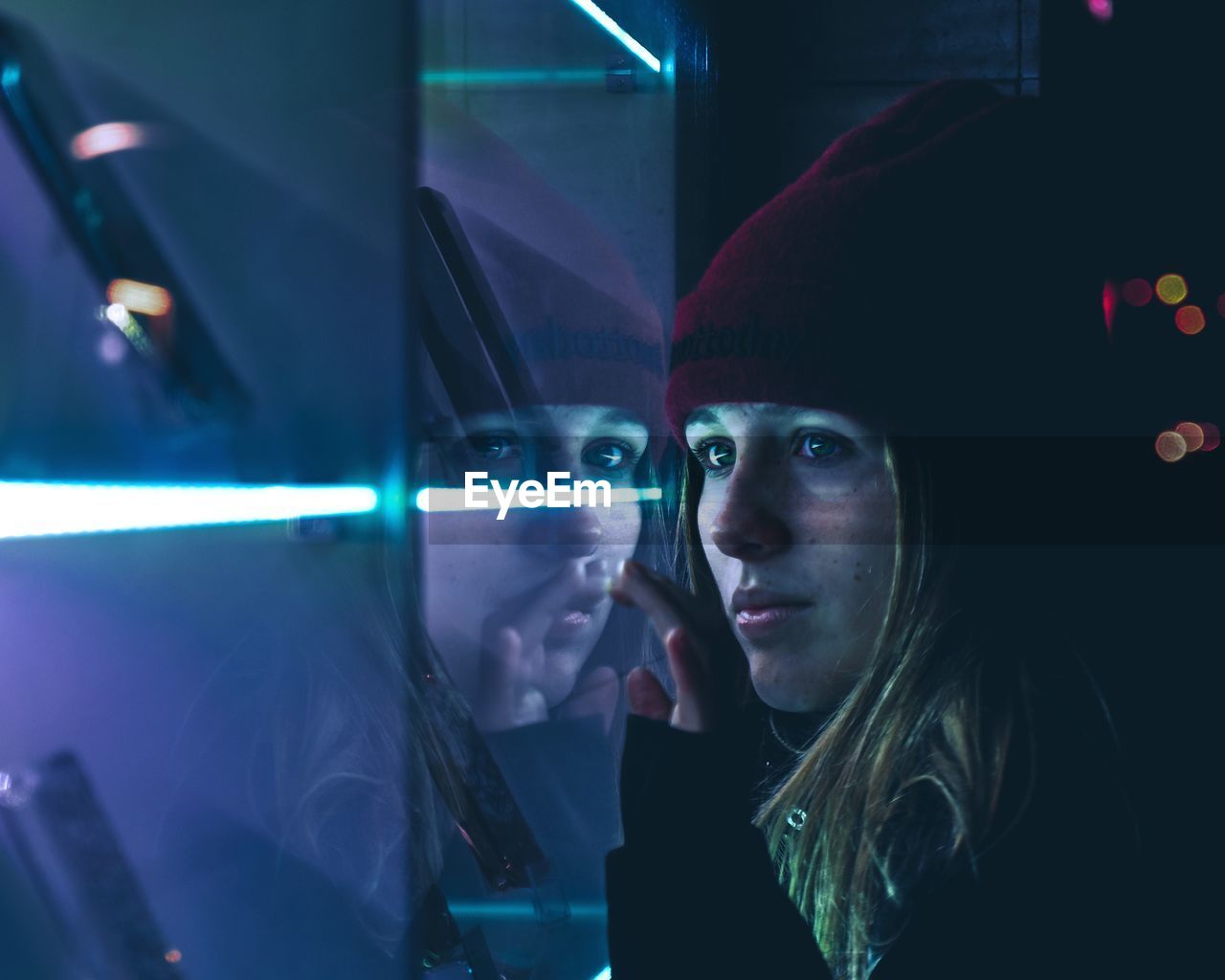 Close-up of young woman looking away by glass window with reflection