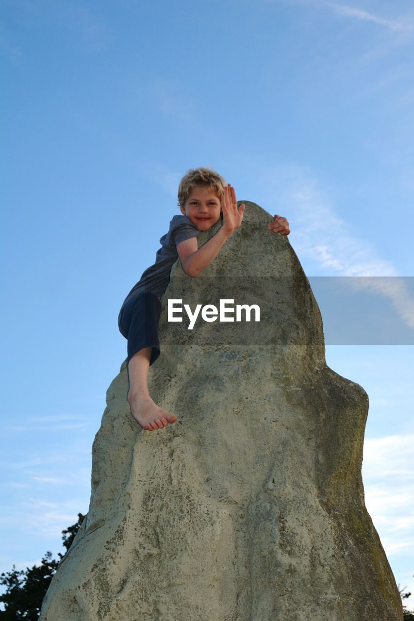 Low angle portrait of boy on rock against sky