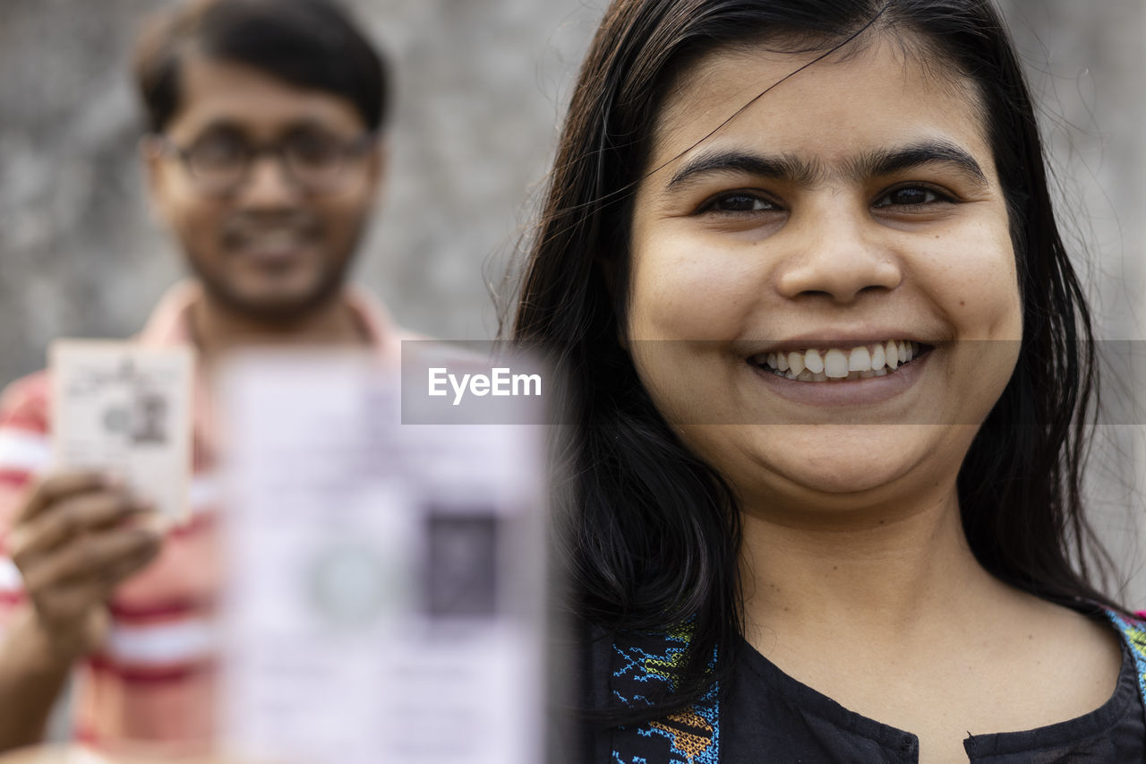 Indian man and woman showing blurred voter card with smile standing in queue