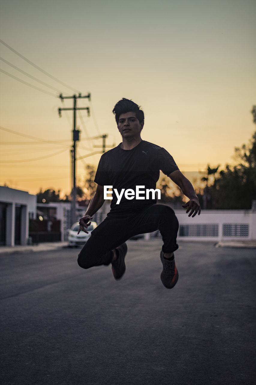 Full length of man jumping on street against sky during sunset