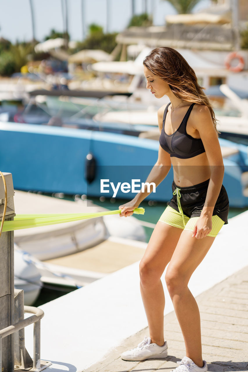 Young woman exercising with resistance band while standing on land