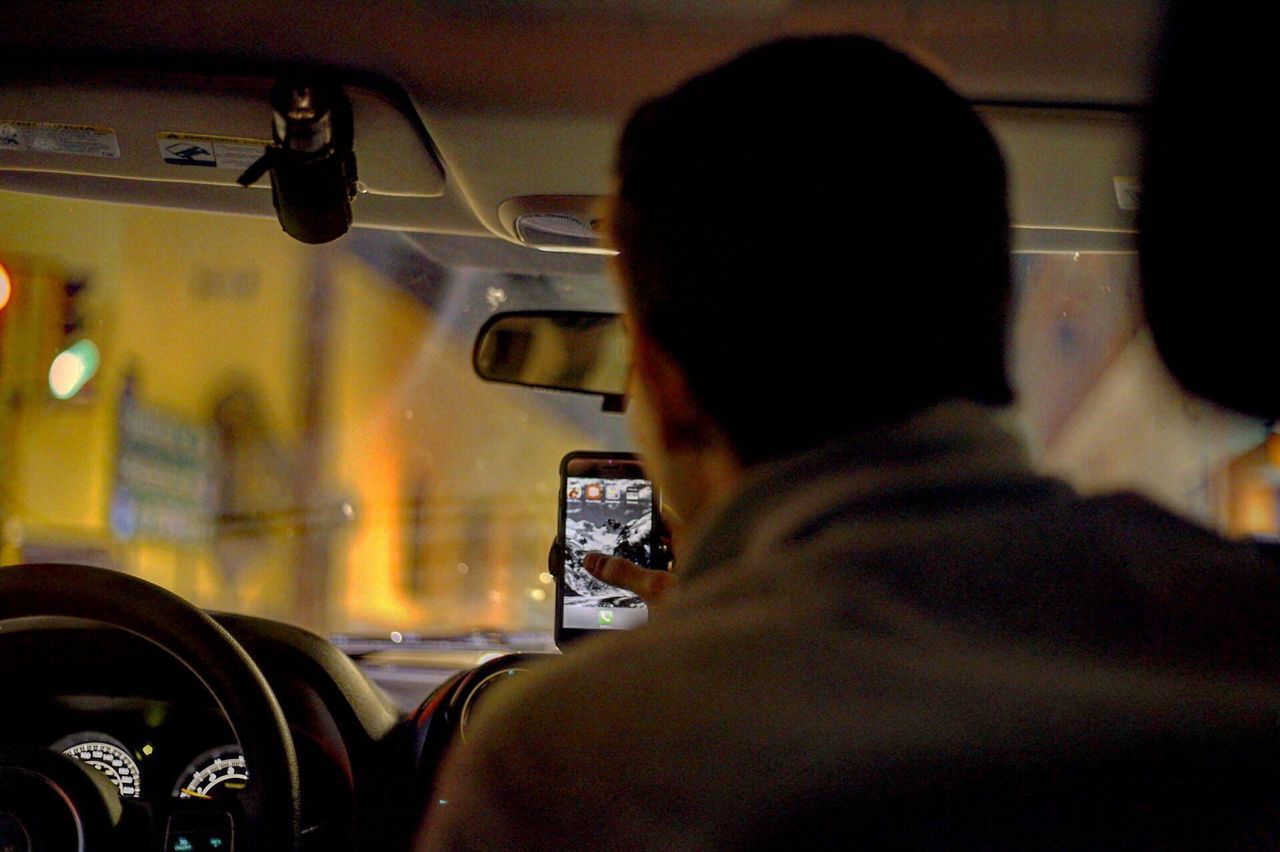 Rear view of man using mobile phone in car