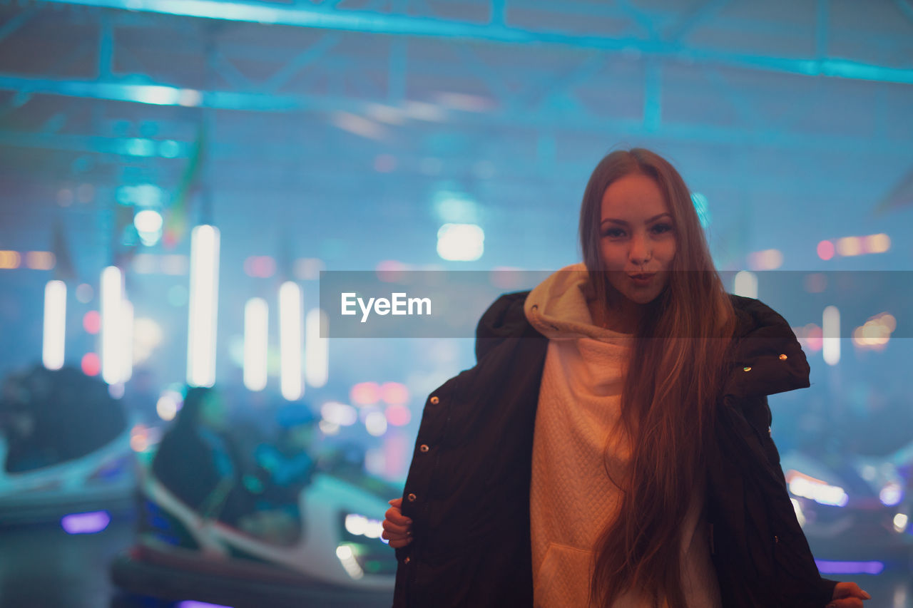 Portrait of young woman standing against illuminated light at night