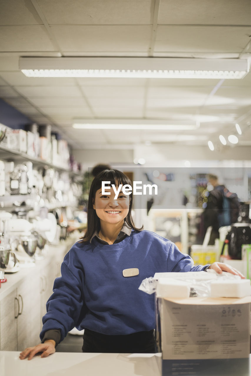 Portrait of smiling saleswoman with appliance standing in electronics store