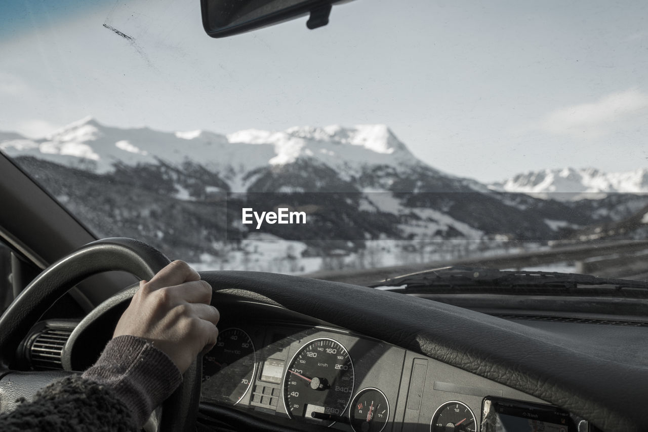 Cropped hand driving car against snowcapped mountains